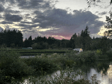 a cloudy sky over a body of water with trees in the foreground