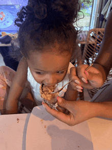 a little girl with curly hair is eating a piece of food with a spoon