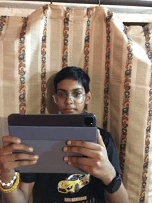 a boy wearing glasses and a black shirt with a yellow car on it holds a tablet