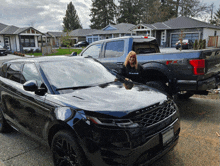 a woman stands in front of a black range rover and a ford f150 truck