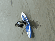 a man is paddling a blue and white paddle board that says all weather on the side