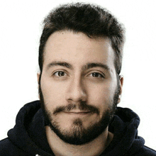 a man with a beard wearing a black hoodie looks at the camera