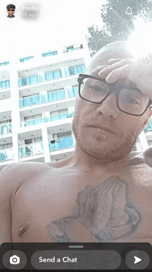 a shirtless man with glasses and a praying hands tattoo on his chest is taking a selfie