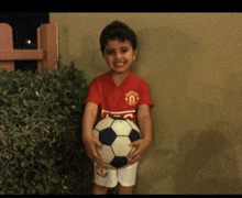 a young boy wearing a red manchester united jersey holds a soccer ball