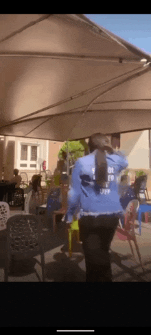 a woman in a blue jacket with the word off on the back is dancing under an umbrella .