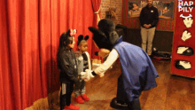 a mickey mouse mascot shakes hands with two little girls in front of a red curtain that says hap pily