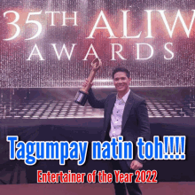 a man in a suit holds a trophy in front of a sign that says 35th aliw awards