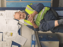 a man wearing a yellow vest is laying on the floor looking at his cell phone