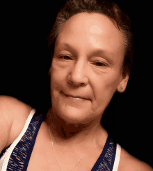 a woman wearing a blue and white tank top and a necklace smiles for the camera