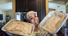 a woman is holding two aluminum foil pans filled with food in her hands .