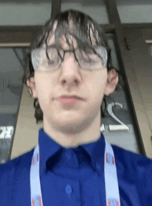 a young man wearing glasses and a blue shirt is standing in front of a window .