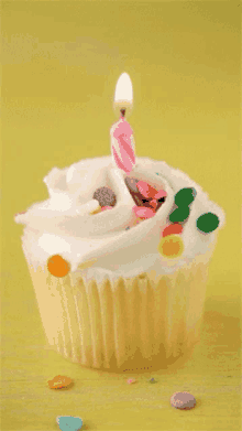 a cupcake with white frosting and sprinkles has a pink candle on top