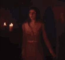 a woman is standing in a dark room with a candle in the background .