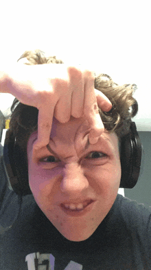 a young man wearing headphones makes a funny face with his hand on his forehead