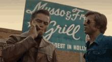 two men smoking cigarettes in front of a sign that says musso & frank grill