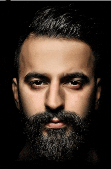 a man with a beard is looking at the camera with a black background