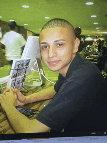 a young man sits at a desk in front of a computer with a picture of him on the screen