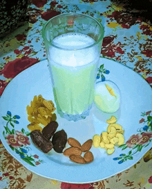 a glass of milk is on a plate with nuts and dates