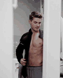 a shirtless man is standing in a doorway with his jacket open .