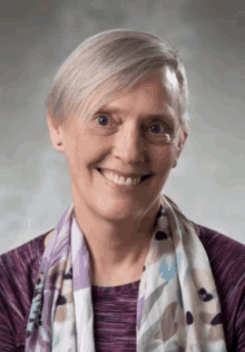 a woman wearing a purple shirt and a purple scarf smiles for the camera