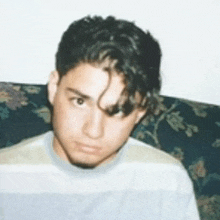 a young man in a striped shirt is sitting on a couch looking at the camera