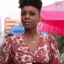 a woman wearing a red and white floral dress and hoop earrings is standing in front of a pink tent .