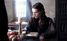 a woman sits at a table with fruit and a candle on it