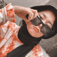 a woman wearing sunglasses and a hijab takes a picture of herself