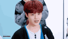 a young man with red hair is wearing a black cardigan and a blue necklace .