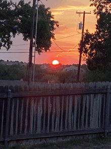 a sunset over a wooden fence with trees in the foreground