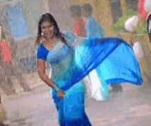 a woman is dancing in the rain in a blue saree .