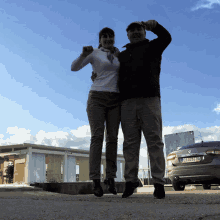 a man and a woman are posing for a picture in front of a car with a license plate that starts with the letter b