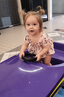 a little girl in a pink dress is playing with a purple toy car