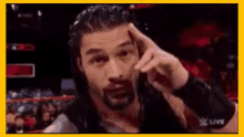 roman reigns is holding his finger to his forehead in a wrestling match .