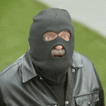 a man with a mustache is wearing a ski mask and a leather jacket .