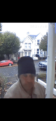 a man wearing a black beanie is standing in front of a white building