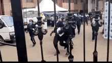 a group of people are dancing in a courtyard behind a fence .