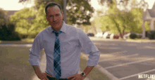 a man in a white shirt and blue tie stands with his hands on his hips in front of a sign that says netflix