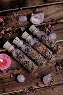 four small bottles filled with various herbs and flowers on a wooden table