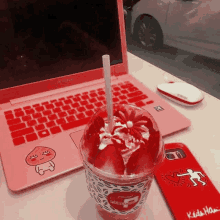 a cup of red ice cream sits next to a pink laptop and a red phone case