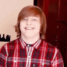 a young man wearing a red plaid shirt is smiling .