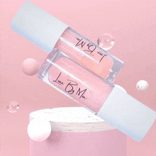 two bottles of lip gloss are sitting on top of a pink podium .