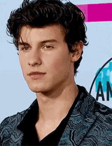 a close up of a young man 's face with curly hair wearing a suit and a black shirt .