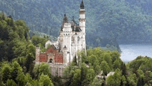 a large white castle sitting on top of a hill surrounded by trees .