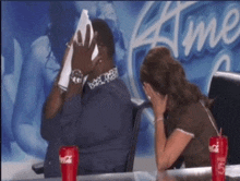 a man is covering his face with a napkin while a woman sits behind him with a coca cola can