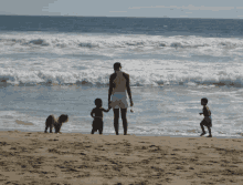 a woman stands on a beach holding two children 's hands