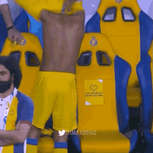 a man in yellow shorts is standing in a locker room with a sign that says do not sit here