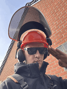 a man wearing a hard hat and headphones salutes in front of a brick building