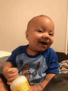 a baby wearing a blue shirt with a baseball player on it is holding a bottle