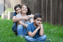 a woman sits on the grass with two boys